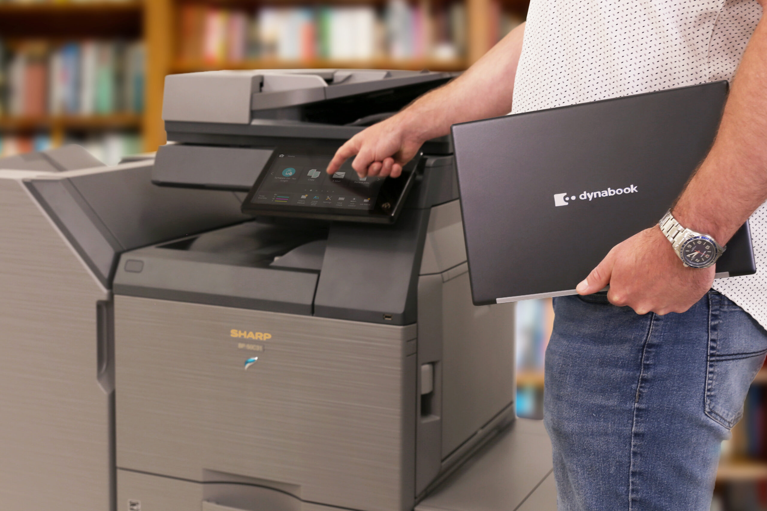 Person operating a Sharp multifunction printer while holding a Dynabook laptop